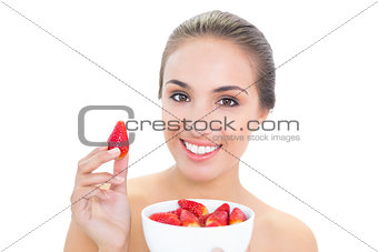 Happy young brunette woman holding up a strawberry