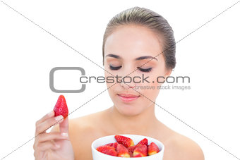 Content brunette woman holding up a strawberry with closed eyes