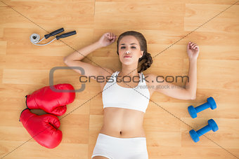 Sporty brunette lying next to jump rope red boxing gloves and dumbbells