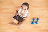 Sporty brunette using a tablet and sitting next to dumbbells