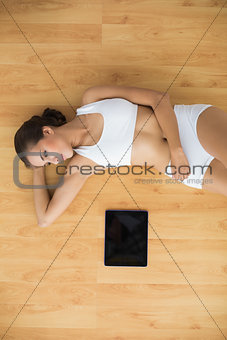 Content sporty brunette lying next to a tablet