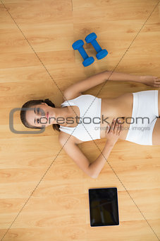 Sporty brunette lying next to a tablet and dumbbells