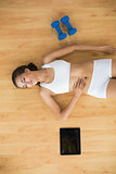 Sporty woman with closed eyes lying next to a tablet and dumbbells