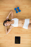Sporty woman lying next to a tablet and dumbbells