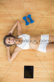 Happy sporty brunette lying next to a tablet and dumbbells