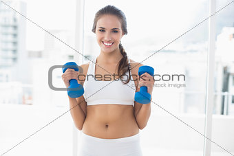 Cheerful sporty brunette holding dumbbells