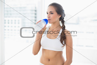 Content sporty brunette drinking from a water bottle