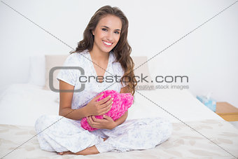 Content attractive brunette holding a heart pillow