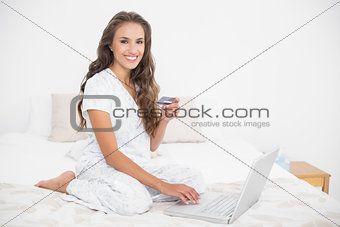 Happy attractive brunette holding credit card and using laptop