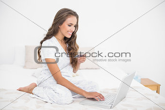 Smiling attractive brunette holding credit card and using laptop