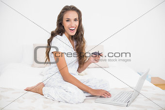 Laughing attractive brunette holding credit card and using laptop