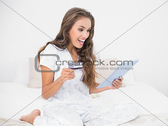 Surprised smiling brunette looking at tablet and holding credit card