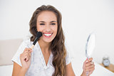 Smiling attractive brunette holding a brush and a mirror