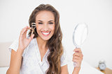 Smiling attractive brunette holding an eyelash curler and mirror