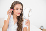 Content attractive brunette applying mascara and holding mirror