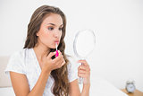 Serious attractive brunette applying lip gloss and holding mirror