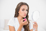 Calm attractive brunette applying lip gloss and holding mirror