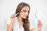 Content attractive brunette using an eyebrow brush and mirror