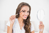Smiling attractive brunette using eyebrow brush and mirror
