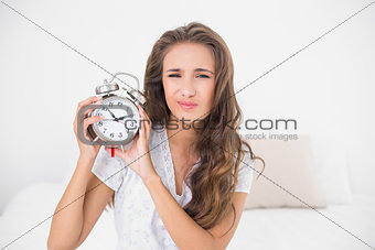 Upset pretty brunette holding alarm clock