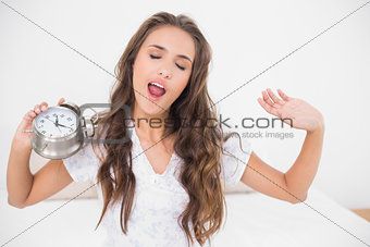 Yawning brunette holding alarm clock