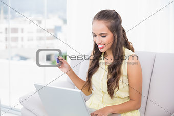 Smiling young brunette using credit card and laptop