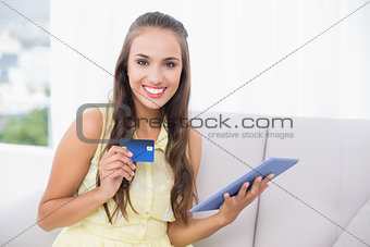 Smiling young brunette holding credit card and tablet