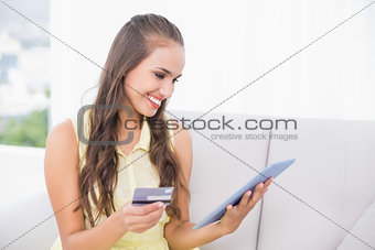 Smiling young brunette looking at tablet and credit card
