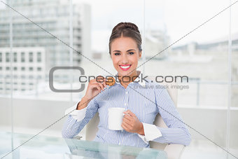 Smiling brunette businesswoman holding mug and cookie