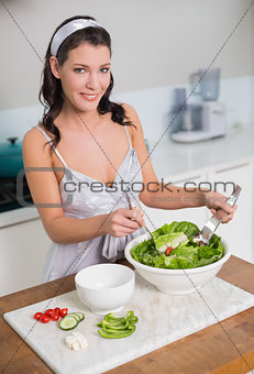 Smiling pretty brunette mixing healthy salad