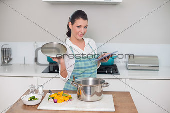 Happy gorgeous woman wearing apron using tablet while cooking