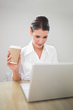 Focused gorgeous businesswoman holding coffee while using laptop