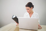 Gorgeous businesswoman working on laptop holding datebook