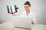 Smiling businesswoman working on laptop holding datebook