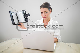 Serious businesswoman working on laptop holding datebook