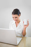Smiling businesswoman working on laptop holding coffee