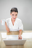 Content businesswoman working on laptop holding coffee