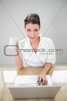Peaceful businesswoman working on laptop holding coffee