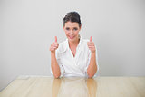 Smiling brown haired businesswoman giving thumbs up to camera