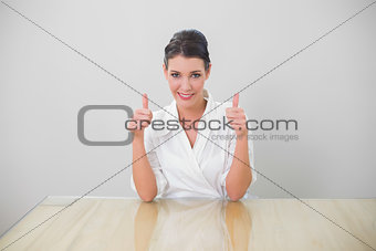 Smiling brown haired businesswoman giving thumbs up to camera