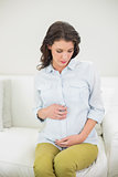 Thoughtful pregnant brown haired woman holding her belly