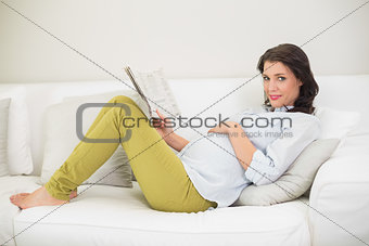 Relaxed pregnant brown haired woman reading a newspaper
