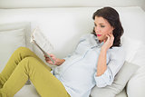 Concentrated pregnant brown haired woman reading a newspaper