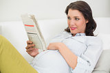 Cute pregnant brown haired woman reading a newspaper