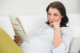Thinking pregnant brown haired woman reading a newspaper
