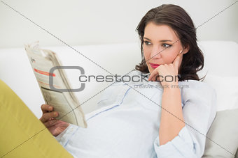 Thinking pregnant brown haired woman reading a newspaper