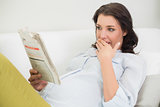 Surprised pregnant brown haired woman reading a newspaper
