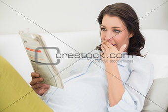 Surprised pregnant brown haired woman reading a newspaper
