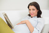 Pleased pregnant brown haired woman reading a newspaper