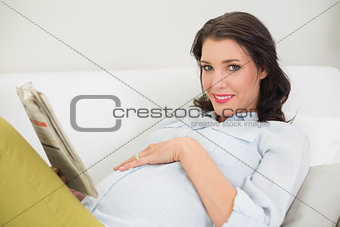 Pleased pregnant brown haired woman reading a newspaper